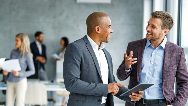 Two leaders discussing work in the foreground with others in the background.