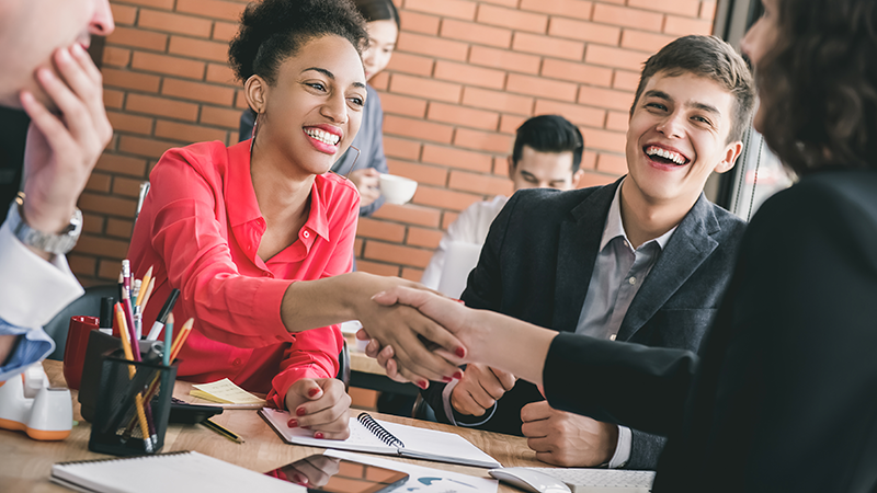 happy woman shaking hands with others smiling looking on.